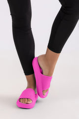 Person wearing bright pink slides with black leggings on a light gray background