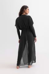 Woman wearing a black long-sleeve dress with sheer panels on a white background